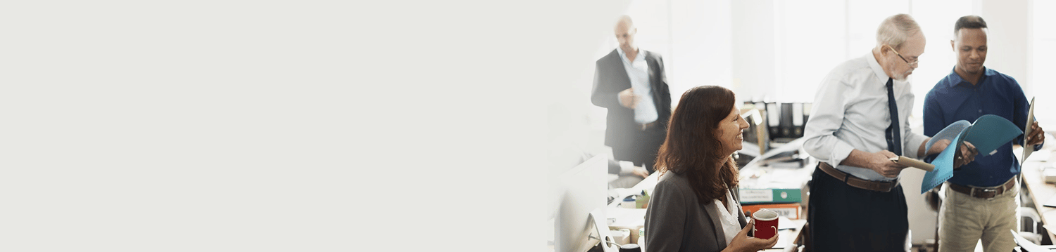 Two men stand together to review report while woman sits next to them with coffee