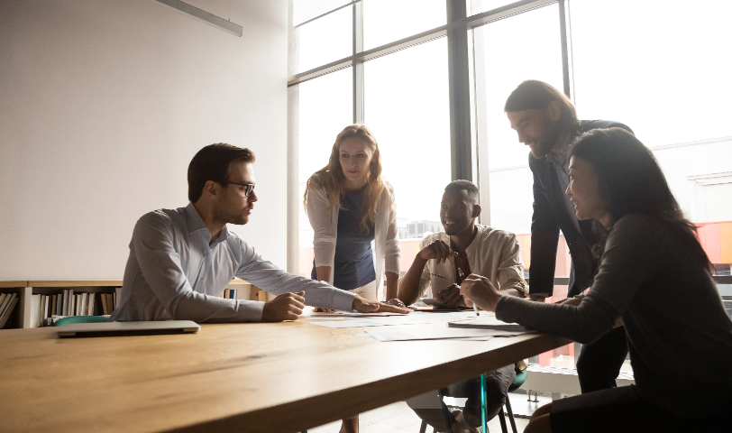 A group of 5 people stand around a table and discuss