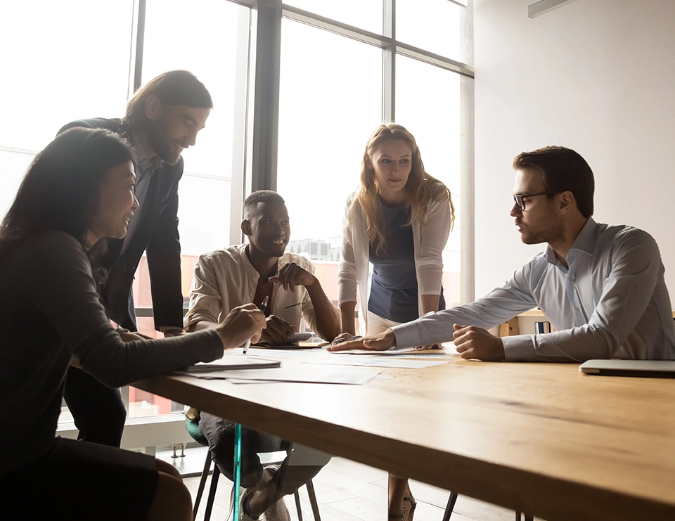 A group of 5 people sit around a table and discuss