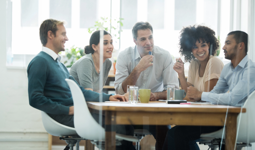 A group of 5 people sit at a table and chat