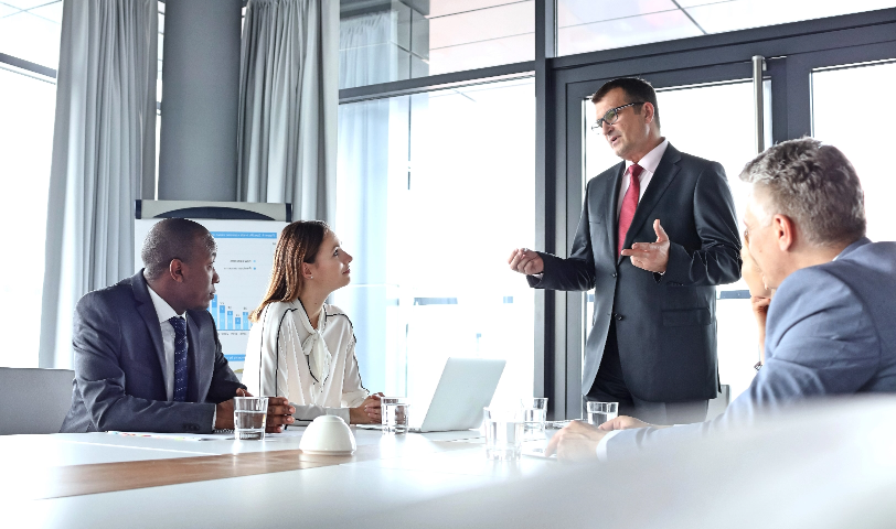 A man stands in front of three others and gives a presentation